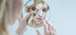 woman looking into broken mirrow representing schizophrenia. Vitamin deficiency